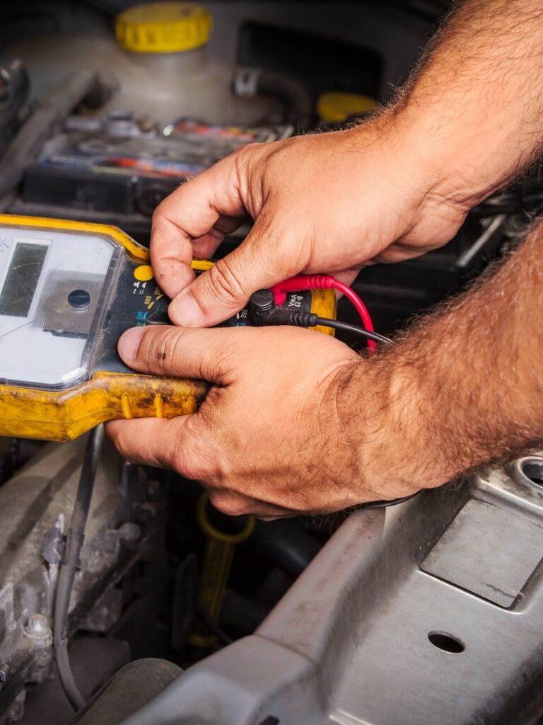 A person is using a multimeter to test electrical components in a car engine.